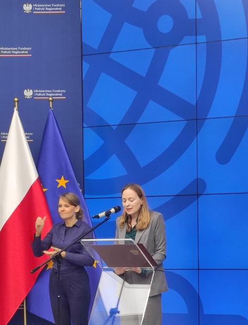 Ministra Funduszy i Polityki Regionalnej, Pani Katarzyna Pełczyńska-Nałęcz przemawia na mównicy, obok niej stoi tłumaczka języka migowego.